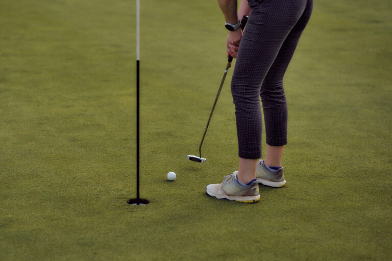 Golfer mit gemusterten Hosen putten während einer Hamburger Unterrichtsstunde zum Loch.