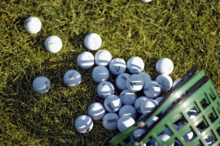Grüner Korb im Gras, verstreute weiße Golfbälle in der Nähe.