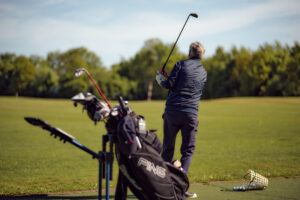 Person schwingt Golfschläger auf der Driving Range; Ausrüstung im Vordergrund.