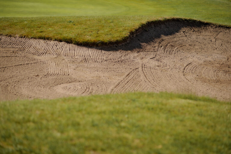 Nahaufnahme des geharkten Sandbunkers, der von gepflegtem Gras umgeben ist.