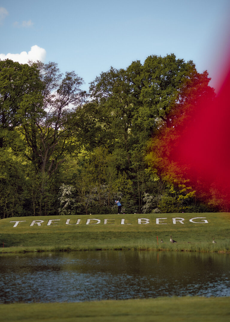Grasbewachsener Hügel mit "TREFUDELBERG", Teich, Bäume, entfernte Person, roter Fleck.