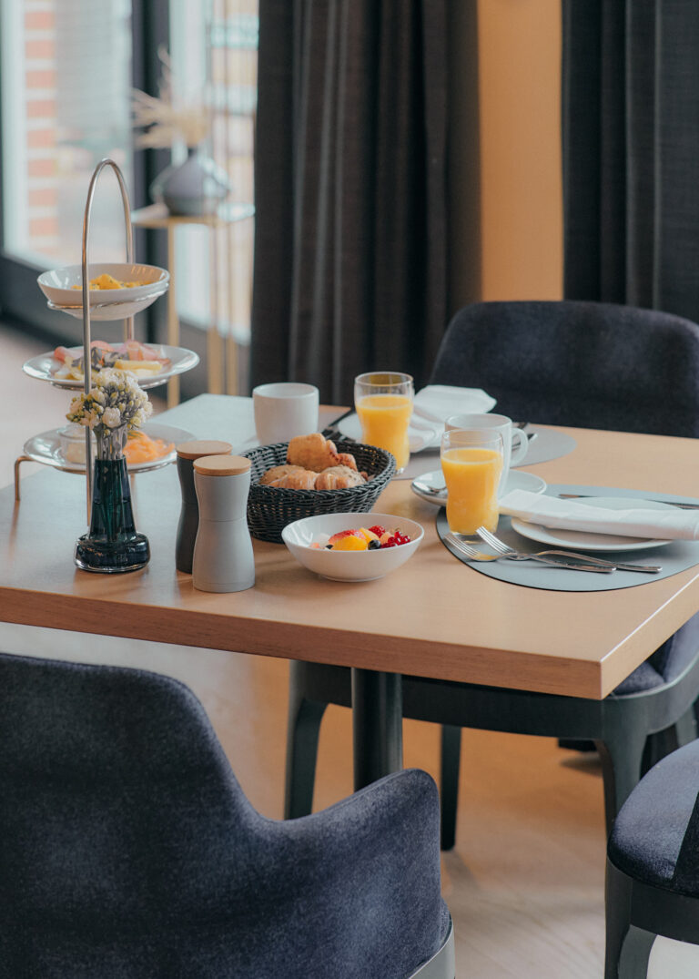 Der Frühstückstisch im Hotel ist mit Speisen, Getränken und Blumen gedeckt.