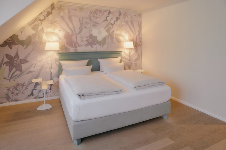 Doppelbett mit weißem Bettzeug, Blumenwand, gemütliche Atmosphäre.