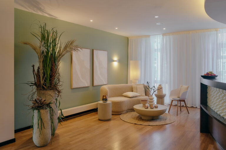Modernes Hotel-Wohnzimmer: grüne Wand, beiges Sofa, helles Holz.