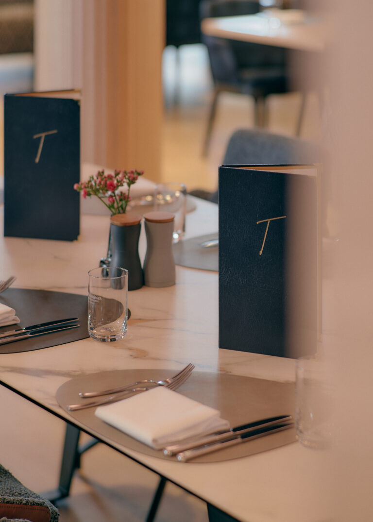 Eleganter Restauranttisch mit Speisekarten, Blumen und Gedecken.