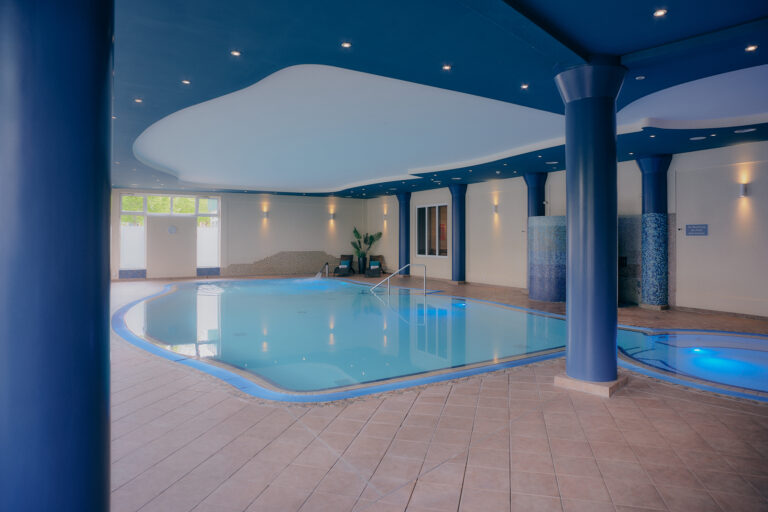Pool des Kurhotels: blaue Säulen, gefliester Boden, Beleuchtung, Pflanzen, Sitzgelegenheiten.