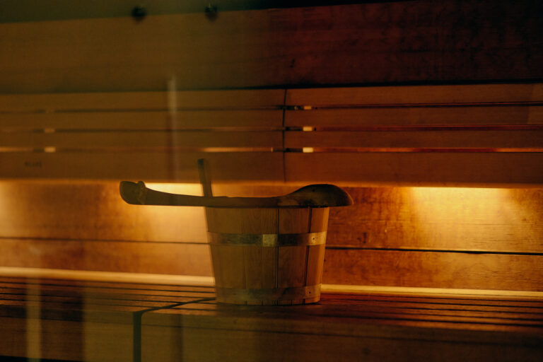 Holzeimer und Schöpfkelle auf der Bank in der warm beleuchteten Sauna.