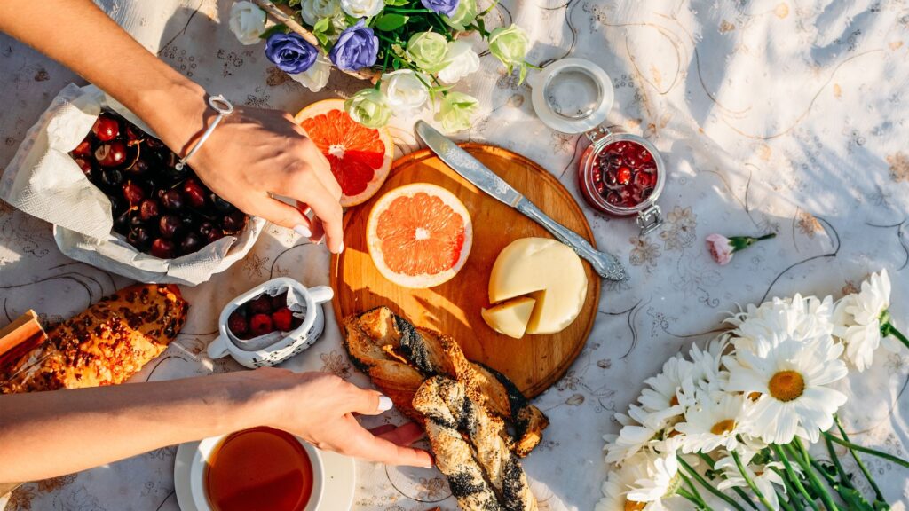 Weißes Picknick auf dem Golfplatz: Obst, Käse, Gebäck, Tee, Blumen.