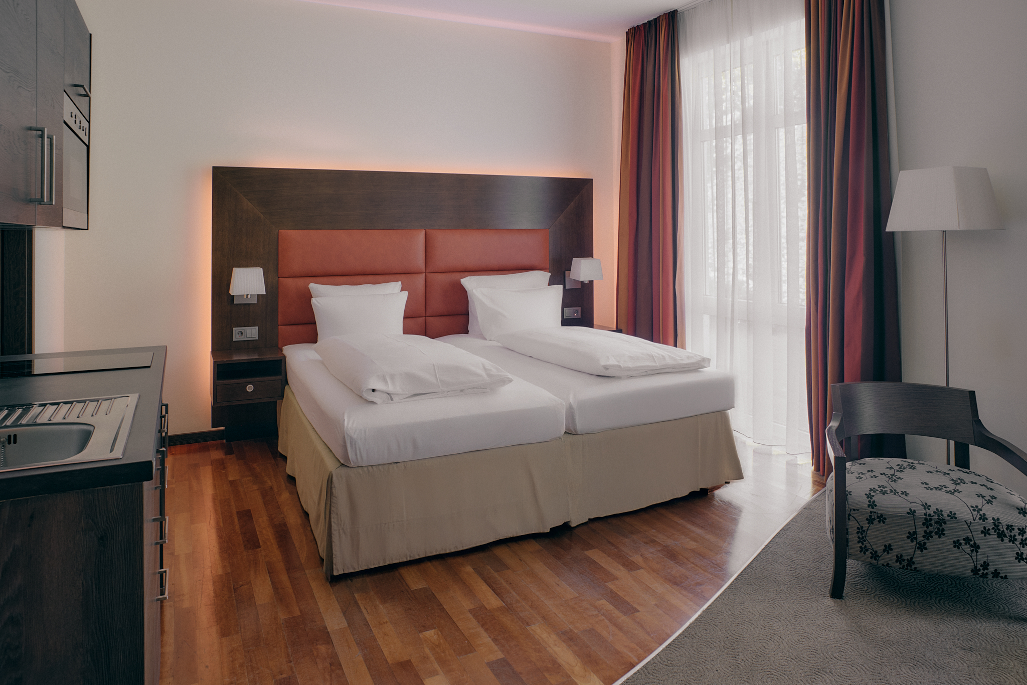 Superior Apartment: Doppelbett, Nachttische, Fenster, Lampe, Stuhl, Kochnische.