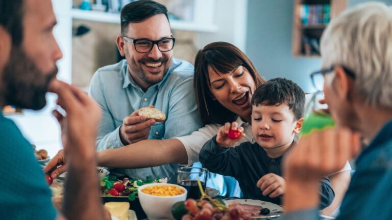 Lächelnde Erwachsene und ein Kind brunchen gemeinsam und genießen frische Lebensmittel.