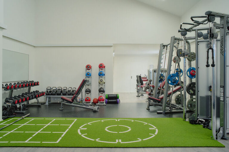 Fitnessraum des Hotels: freie Gewichte, Bänke, Maschinen, Rasen; sauber, hell.