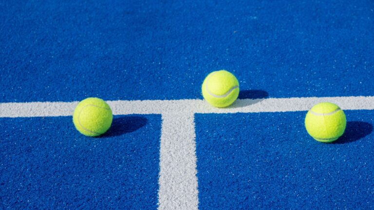 Drei gelbe Tennisbälle liegen neben einer weißen Linie auf dem Spielfeld.