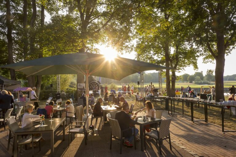 Menschen speisen unter Sonnenschirmen und genießen die Sonne in der Nähe eines Hamburger Hotels.