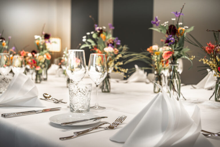 Formal-dining-table-set-elegant-weiß-servietten-glassware-floral-arrangements bereit für eine Mahlzeit in elegantem Rahmen.