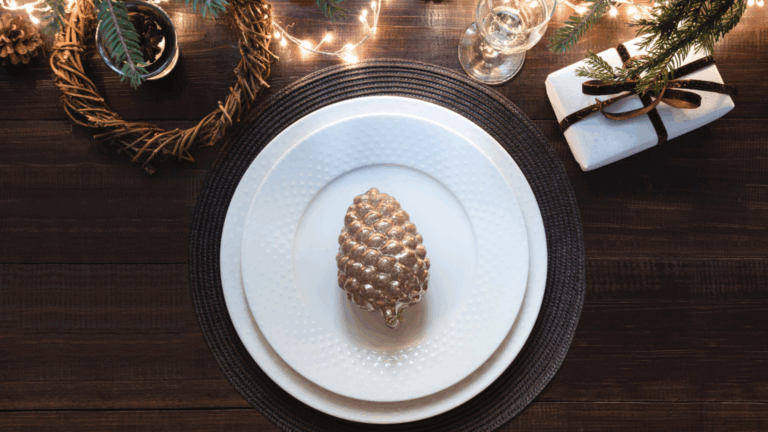 Holiday-table-setting-Christmas-brunch shows a decorated table with pine cones, gift, placemat, wreath, champagne glass and fairy lights.