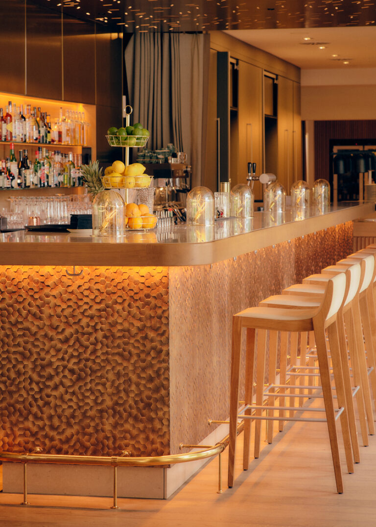 Modern-bar-verfügt über einen beleuchteten Tresen, Holzhocker, Spirituosenregale und einen festlichen Zitrusfruchtstand.